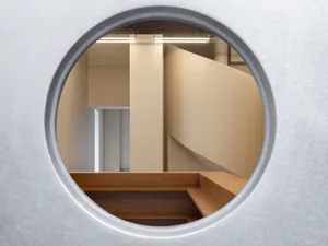 A perspective view of a staircase made of wood, leading to another level through a round window, with a sense of depth and dimension in the space