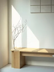 A wooden table with a vase sits in a serene indoor space surrounded by two trees and natural elements