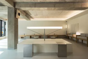 Bright and inviting open space with a large white table, chairs, and natural light, featuring concrete walls