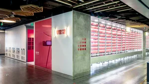 A modern interior design showroom with a red accent wall, white walls, and a large window, featuring several chairs and a mounted TV