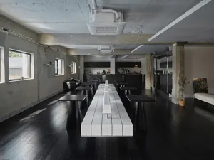 空蕩蕩的現代餐廳，配有長形白色餐桌與黑色地板，周圍環繞座椅，並由自然光與人工照明充足照亮