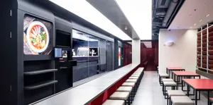 Industrial kitchen with modern black cabinets, red accents, and a long counter with chairs and two TVs mounted on the wall