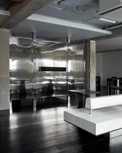 Open modern living area with a white couch in front of a glass wall, two dining tables, and comfortable seating for three, with a focus on clean lines and minimalistic design elements