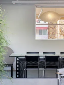 A modern dining area with a glass table surrounded by black chairs and a potted plant, featuring clean lines and minimalistic design elements