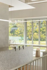 Modern kitchen with large windows, sleek countertops, stainless steel appliances, and two sinks for multiple users