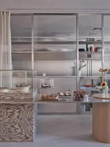 Modern restaurant kitchen with stainless steel appliances and surfaces, a counter with displayed food items, and a contemporary atmosphere