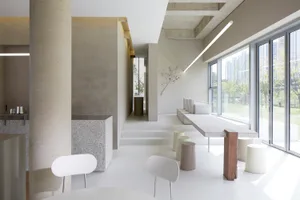 Open living area with a white table surrounded by chairs, benches, and a potted plant, featuring a clean and minimalistic atmosphere