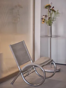 A modern room with a gray metal chair on a hardwood floor, surrounded by vases and potted plants