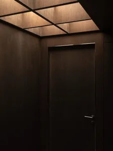 昏暗燈光下的走廊中，一扇帶有金屬把手的深色木門，營造出親密溫馨的氛圍