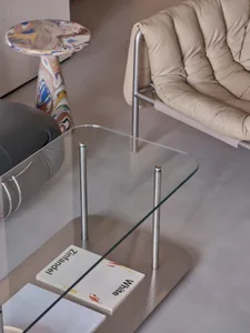 Cozy modern living space with a glass coffee table on a grey carpet, two chairs, and a book, creating a clean and contemporary atmosphere