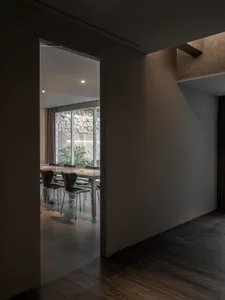 Empty dining area with a large table and chairs in a white-walled room, adjacent to a kitchen