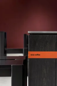 A black wooden coffee table with a red label on its side sits in front of a red background wall, showcasing its sleek design