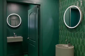 Bathroom with two sinks under round lights, green walls, and a door, creating a modern and unique space