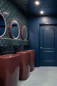 Bathroom with three sinks, dark blue walls, and a doorway, creating a clean and functional space with a touch of elegance