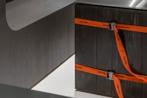A wooden cabinet with orange straps and a brown finish is part of a kitchen area with two sinks, creating a warm and cozy atmosphere with natural materials and water elements