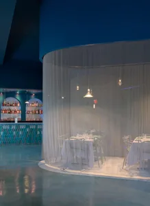 A restaurant interior with a curved bar wall and multiple dining tables, chairs, and a relaxed atmosphere