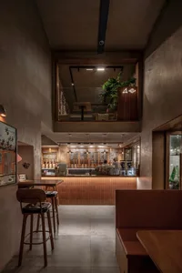 A restaurant interior with wooden floors and walls, featuring comfortable seating and dining tables with bottles and chairs