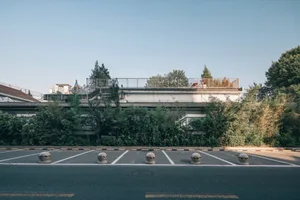 A modern building with a metal roof, surrounded by a parking lot with cars and chairs, suggesting a public or commercial space
