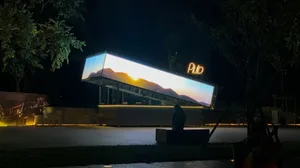 A nighttime building facade with a large window display showcasing a sunset view, accompanied by two benches and a calm atmosphere