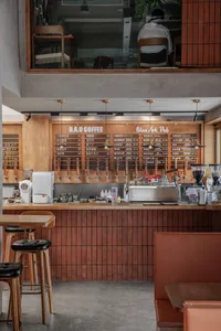 A casual coffee shop interior with a wooden bar, stools, and chairs, featuring bottles and cups, and a welcoming atmosphere