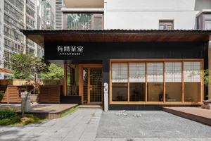 Modern Asian restaurant with a black facade, wooden elements, and natural light from windows, featuring a dining area with tables and chairs and potted plants
