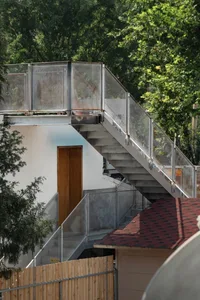 A modern house with a metal staircase leading to a doorway on the second floor, with an open doorway revealing the interior and a calm, inviting atmosphere