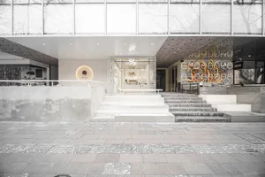 A modern commercial building with a large glass doorway, white frame, and two staircases leading upwards, giving off a sleek and modern vibe