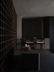 Darkly lit living area with wooden chairs, stone countertop, fireplace, and vases, featuring a dining table and cozy atmosphere