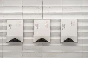 Three white boxes mounted on a wall, each containing small black objects, arranged in a row with one box above the other two