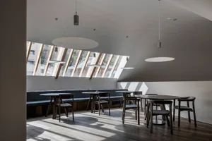 A well-lit restaurant interior with multiple tables, benches, and chairs, featuring natural sunlight and an inviting atmosphere