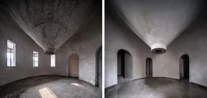 A large, empty room with a vaulted ceiling, arches, and a stone wall, showcasing a minimalist space with no furniture or objects