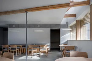 A warm and inviting restaurant interior with wooden tables and chairs, a bar area, and benches, creating a comfortable space for dining and socializing