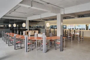 A spacious restaurant interior with a large wooden dining table surrounded by metal chairs, creating a modern and minimalist atmosphere