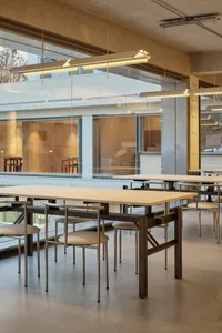 Open modern living space with a glass wall separating two rooms, featuring a dining area and a living space with multiple chairs and natural light