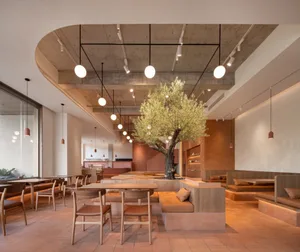 Open restaurant interior with multiple tables, benches, and a tree, featuring warm and inviting atmosphere