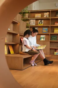 Two women reading together in a well-stocked library with bookshelves and a calm atmosphere