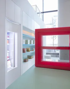 Modern showroom with red door, white walls, and various products on display, including bottles and refrigerators