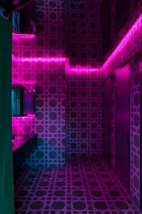 Bathroom with checkered patterned walls, pink and purple tiles, a sink, and a door