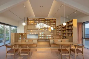 Cozy library interior with wooden floors, bookshelves, comfortable seating, and multiple tables for reading or working