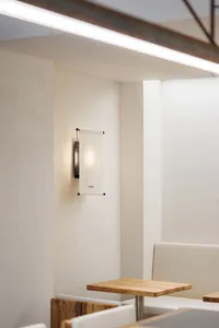 A modern interior space with a white wall, concrete material, and two light fixtures, one on each side of the wall