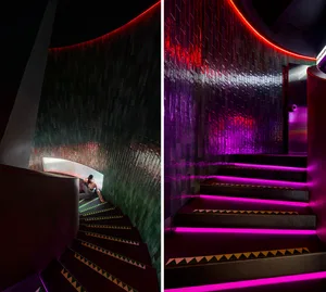 A modern spiral staircase with purple lights illuminating the stairwell, showcasing a sleek metal design