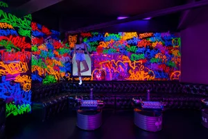 A room with graffiti on the walls and ceiling, featuring two couches and a person standing near the right edge, with a creative and eclectic atmosphere