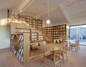 A warm and inviting bookstore interior with wooden floors and walls, featuring bookshelves, a dining table, and comfortable seating