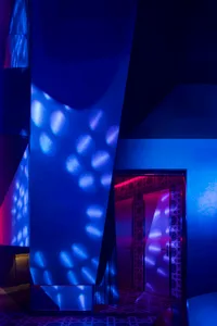 A blue-painted hallway with a door and window, illuminated by glowing lights and ambient atmosphere