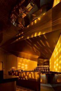 A warm and inviting bar area with a wooden counter, bottles, and cups, creating a cozy atmosphere for guests to enjoy drinks