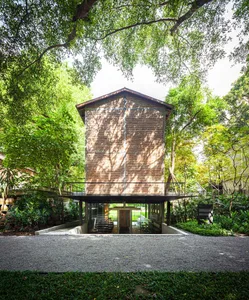 A modern building with a brick exterior, surrounded by trees and greenery, featuring a large window and blending modern and traditional architecture