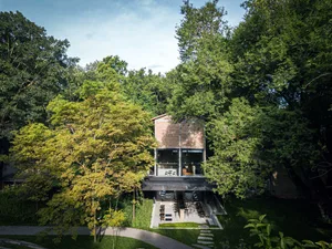 A modern house surrounded by trees in a forest, with large windows and a concrete exterior, set in a peaceful and serene environment