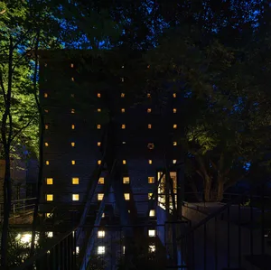 Modern building with a brick exterior, metal staircase, and windows on multiple levels, surrounded by potted plants and captured during dusk