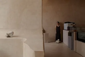 An empty room with a woman standing in front of a brown wall, creating a quiet and peaceful atmosphere
