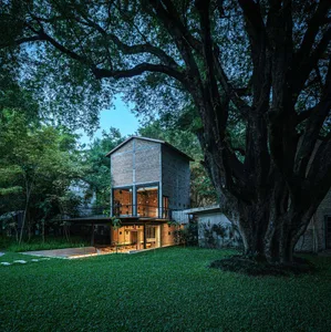 A brick house surrounded by trees, with a large tree in front and natural light entering through the windows